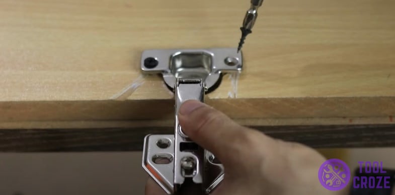 Secure cabinet door hinge on new screw anchors with electric drill and screws